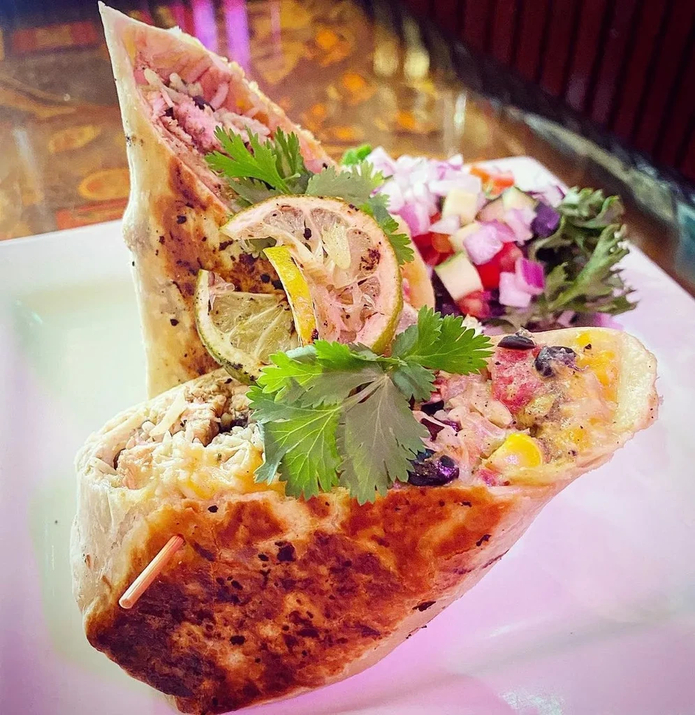 Colorful burrito halves on white plate with salsa and grilled lime.