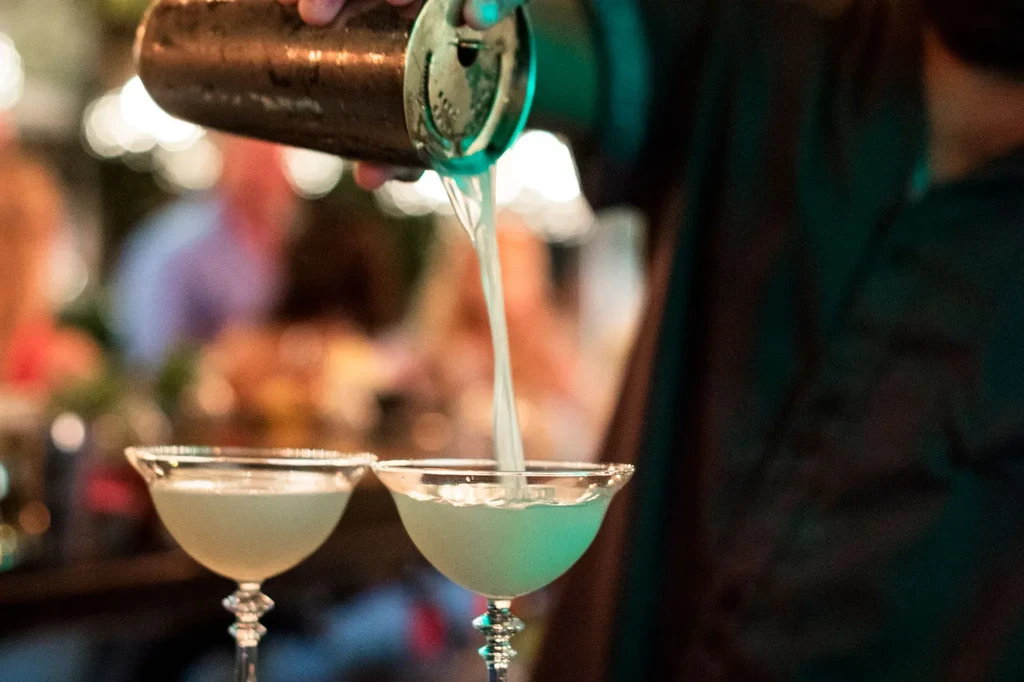 Bartender pours a cocktail from a shaker into a glass.