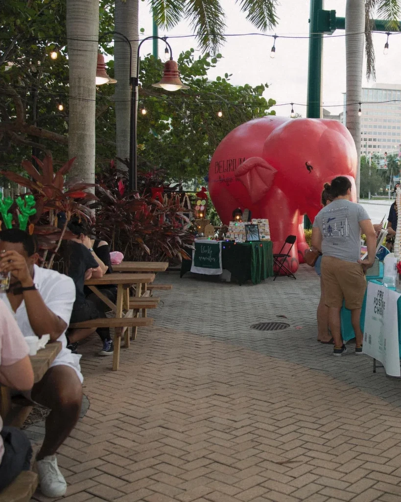 Outdoor market with people, vendor stalls, and a red elephant inflatable.