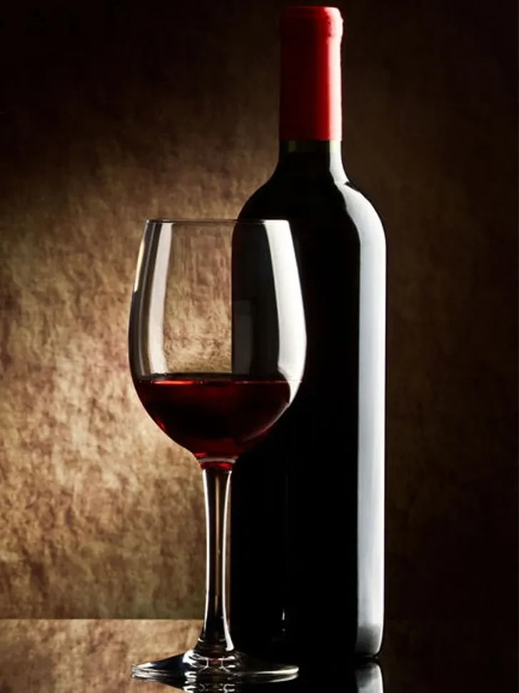 Dramatically lit still life of a wine bottle and glass of red wine.
