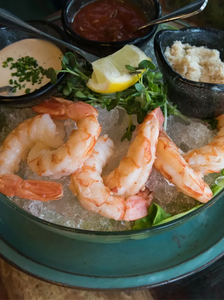 Shrimp cocktail on ice with three sauces, lemon, and microgreens.