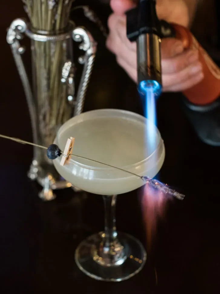Hand torches unique cocktail garnish, creating a small flame effect.