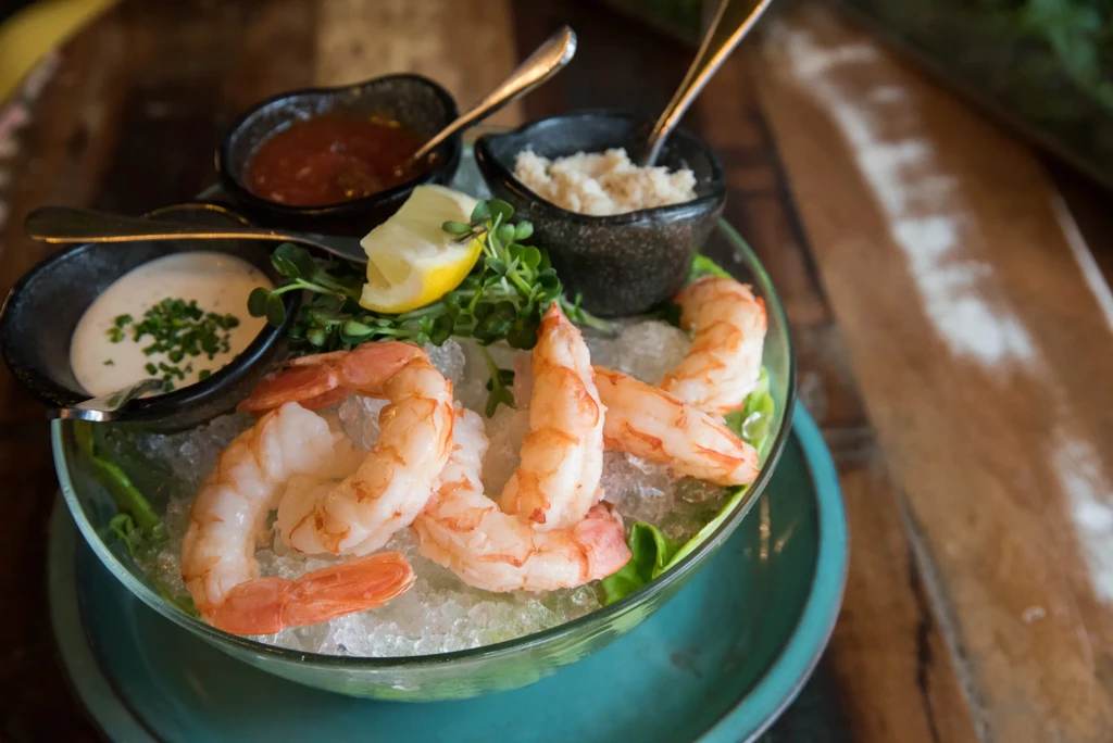 Cooked shrimp cocktail with lemon, ice, and three accompanying sauces.