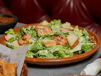 Caesar salad with grilled shrimp, croutons, and cheese in a rustic bowl.