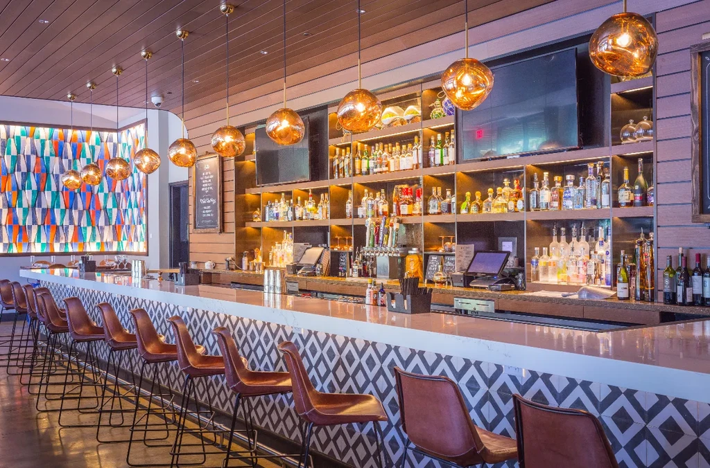 Modern bar with patterned counter, illuminated shelves, and colorful wall.