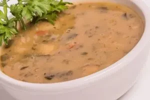 Close-up: Creamy beige soup with flecks in white bowl, garnished with herbs.