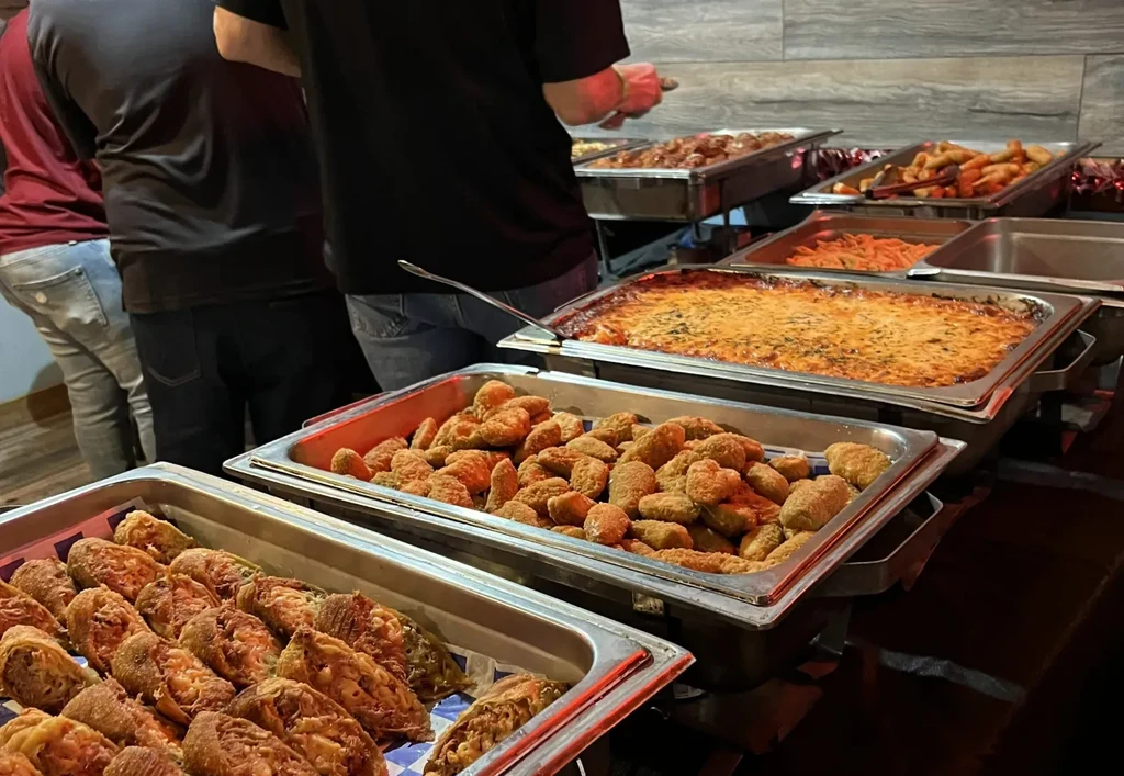 Bustling buffet line with fried appetizers, cheesy pasta, meatballs, and people.