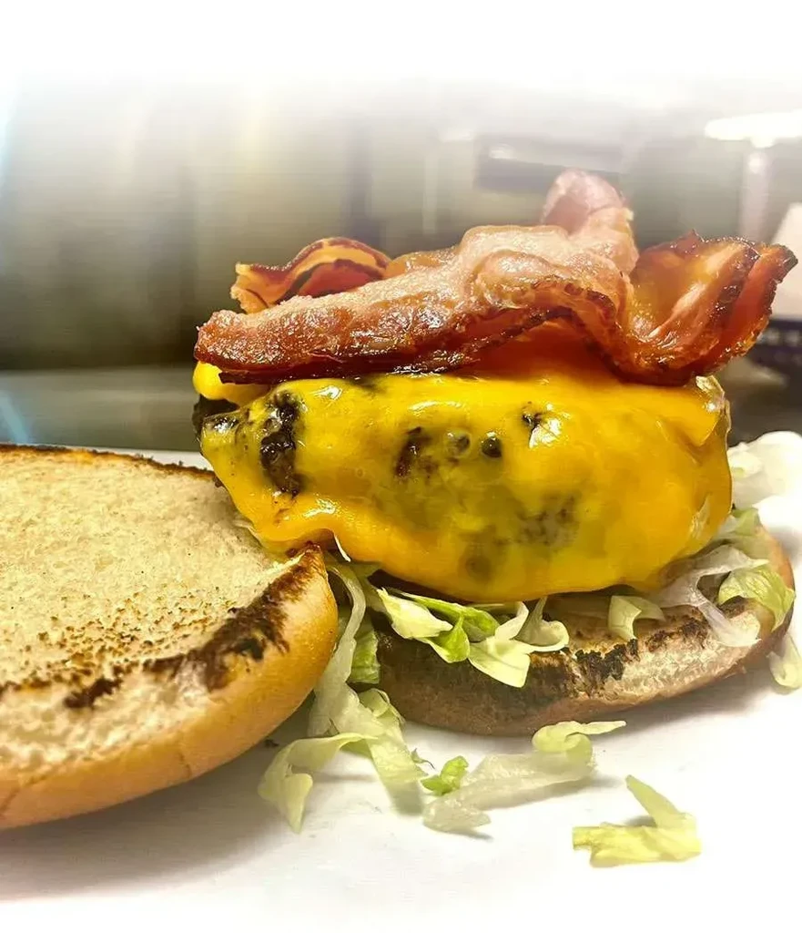 Open-faced burger with beef patty, melted cheese, bacon, and lettuce.