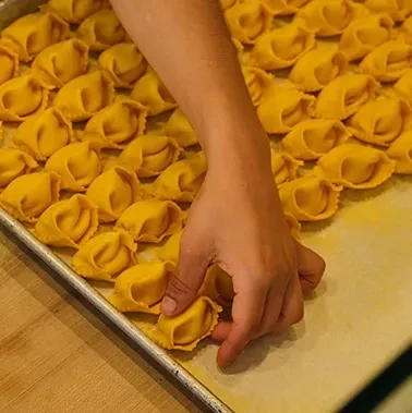 Hand arranging freshly made golden tortellini on a baking sheet.