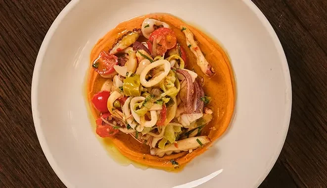 Plated calamari, octopus, and vegetables over orange purée.