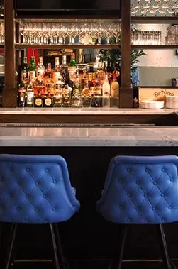 Two empty blue bar stools facing a well-stocked bar.