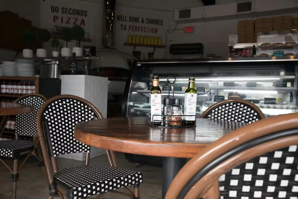 Pizzeria interior with round table, checkered chairs, and a large pizza oven.
