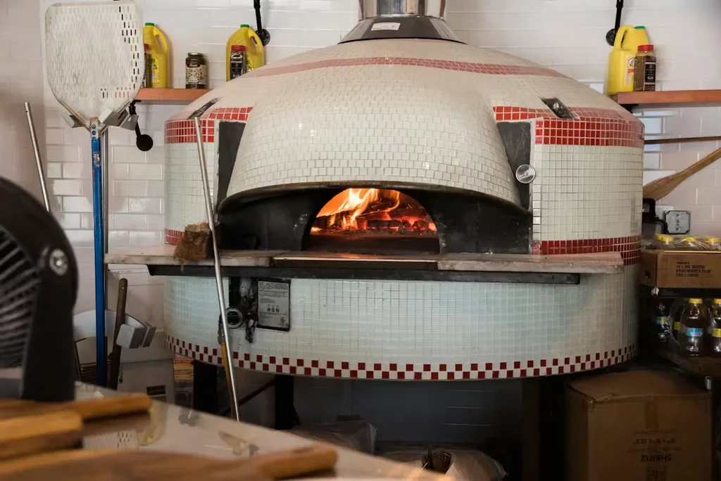 Tiled wood-fired pizza oven with red checkerboard details and active flames.