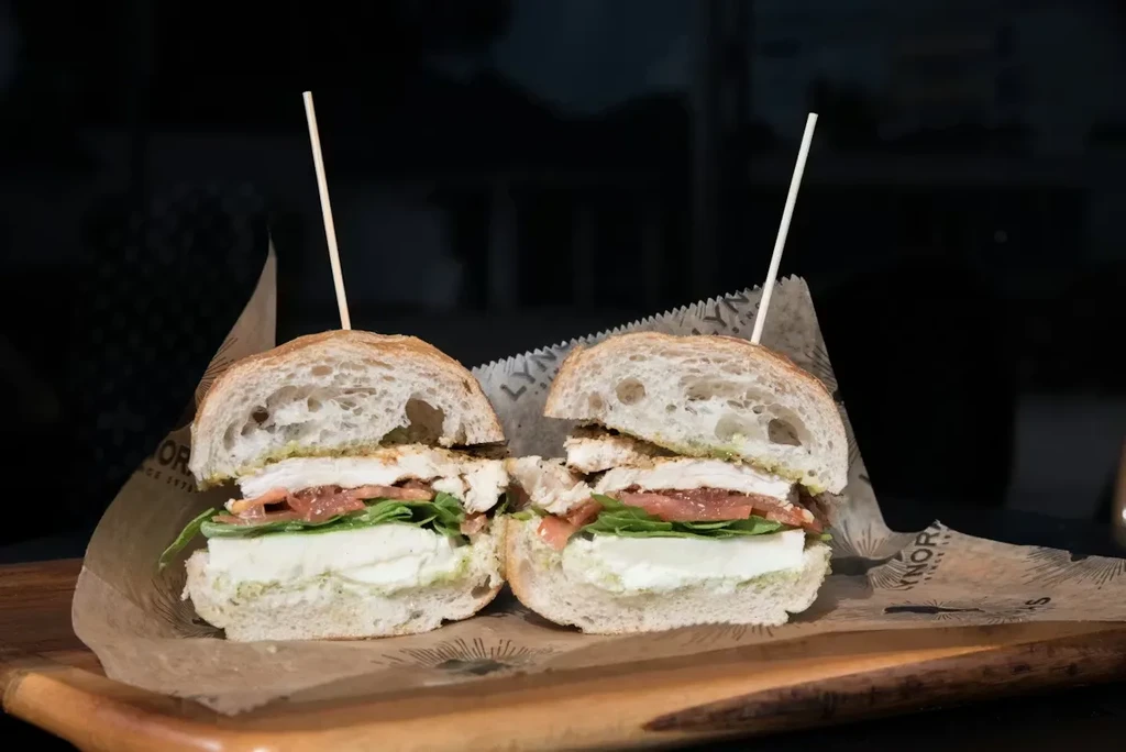 Sandwich halves with chicken, mozzarella, pesto on a rustic board.