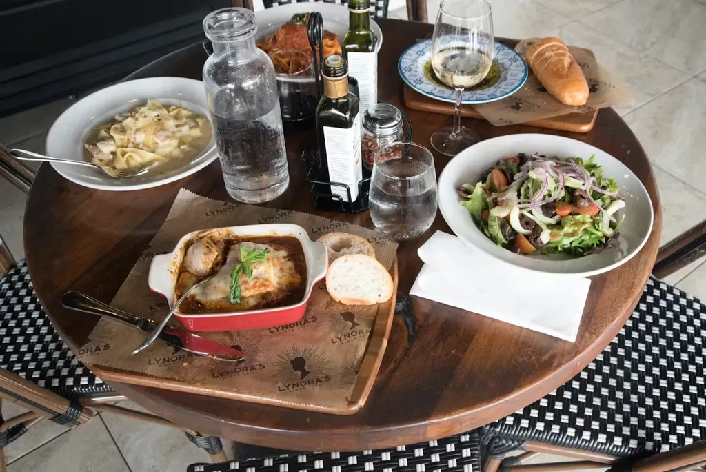 Overhead view: Lynora's table set with pasta, salad, wine, and baguettes.