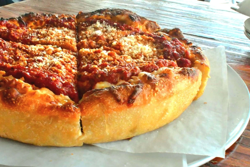 Deep-dish pizza, thick golden crust, red sauce, grated cheese, two slices cut.