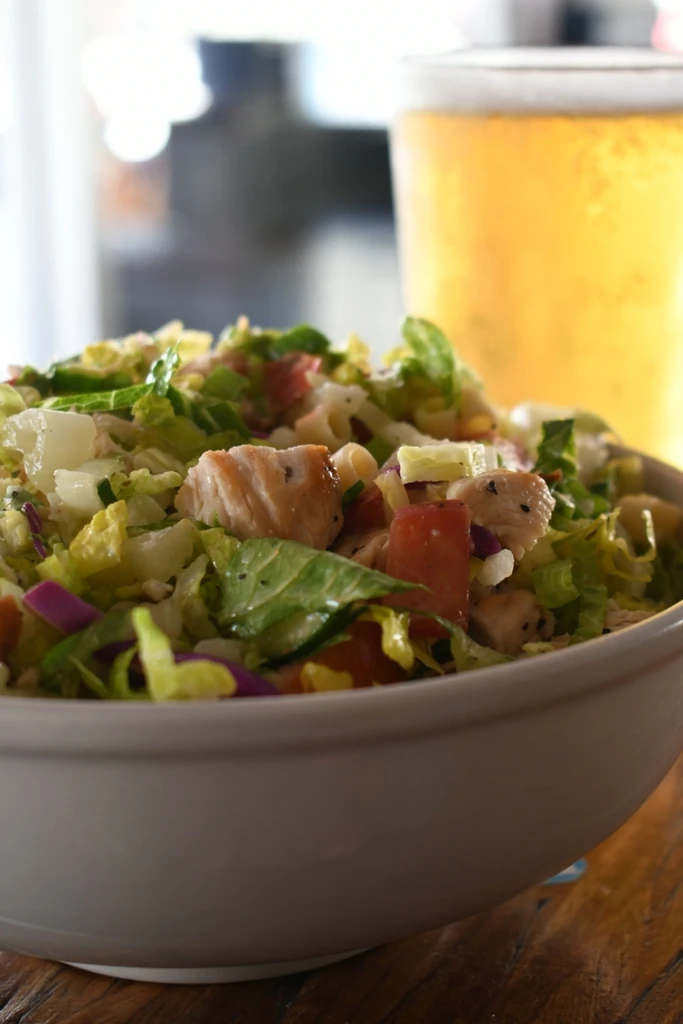 Close-up of fresh salad with greens, chicken, tomato, pasta.