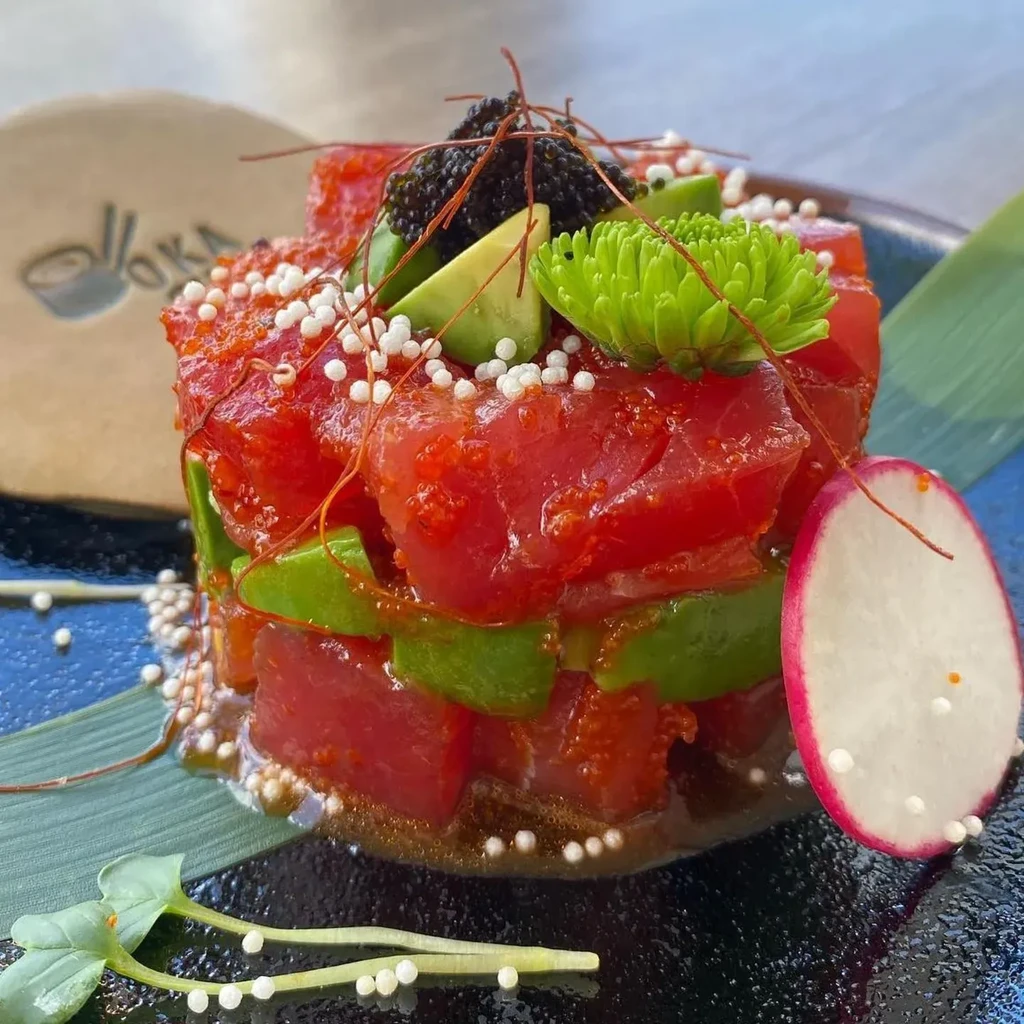 Vibrant tuna and avocado stack, topped with caviar on dark plate.