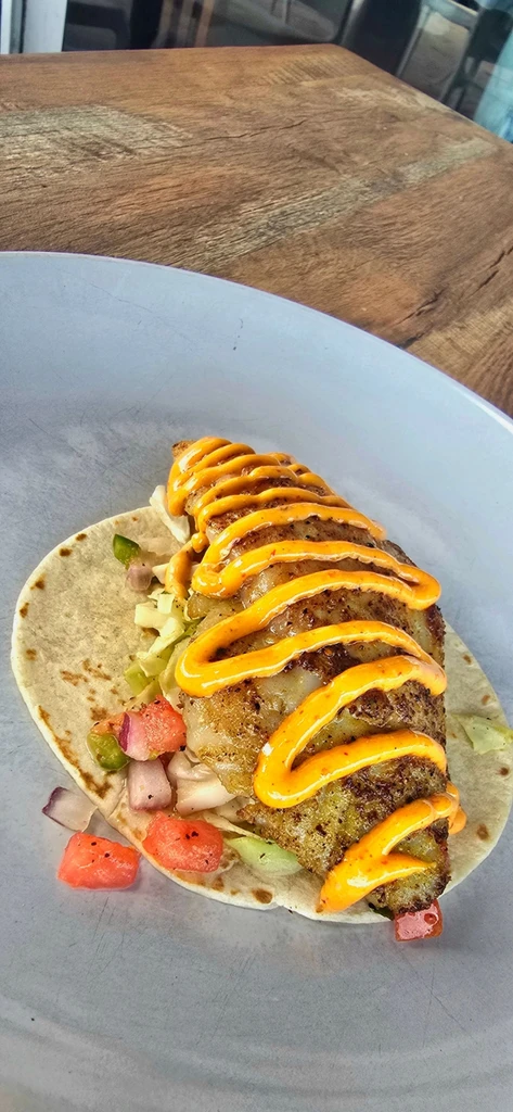 Golden-brown fried fish taco with orange sauce and colorful vegetables.