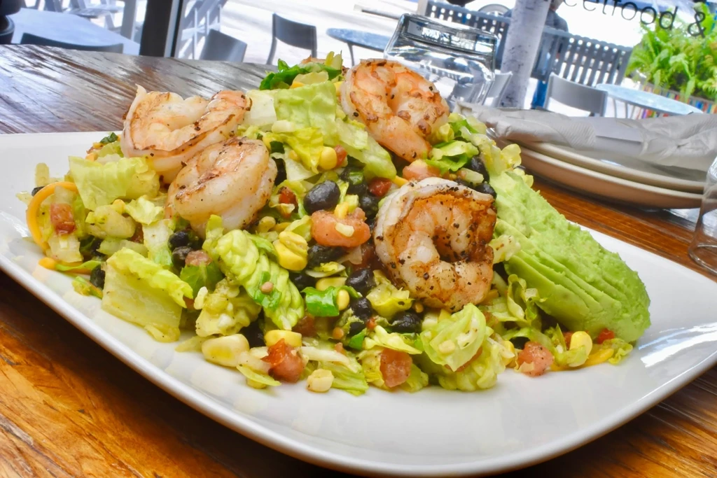 Shrimp salad with avocado, black beans, and corn on a wooden table.