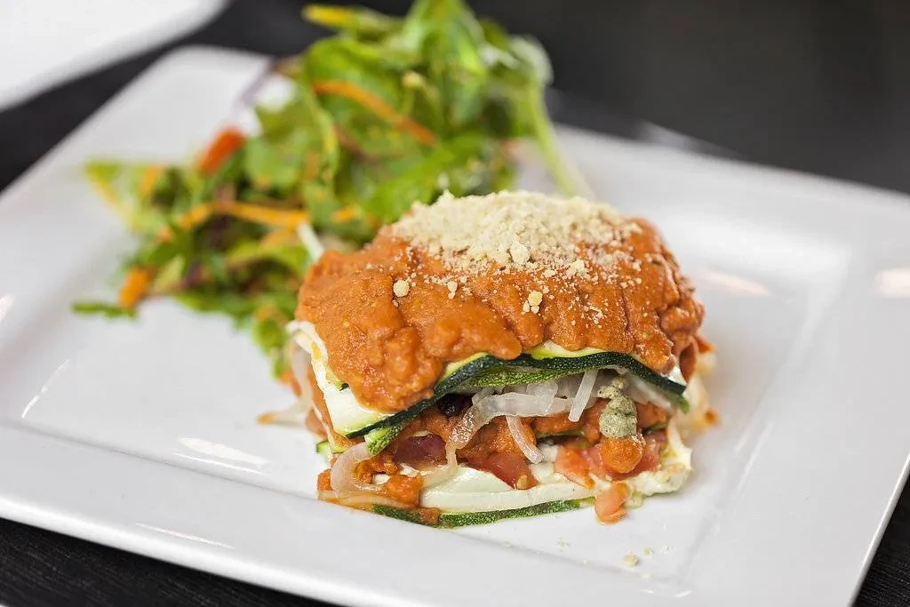 Savory layered dish with zucchini, red sauce, cheese, and mixed greens.