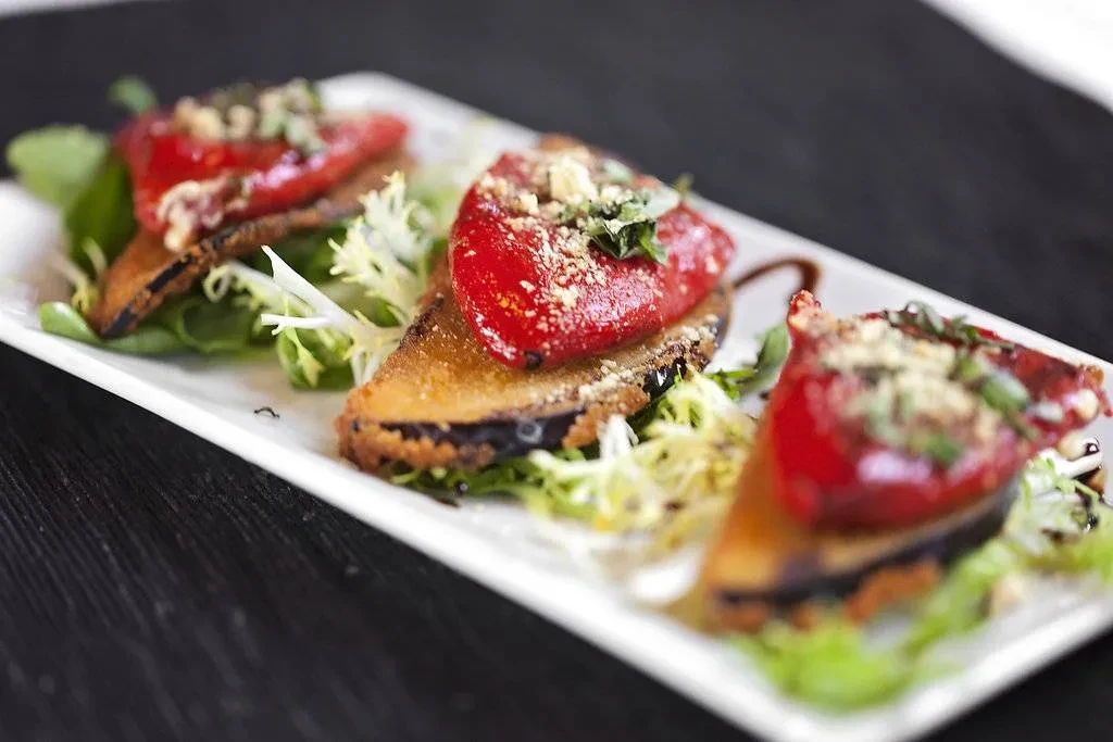 Three fried eggplant appetizers with red bell peppers, herbs, and mixed greens.