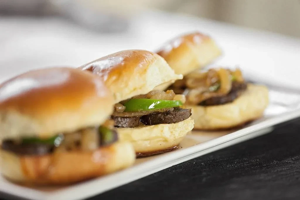 Three sliders with bell pepper and onions on a white plate.