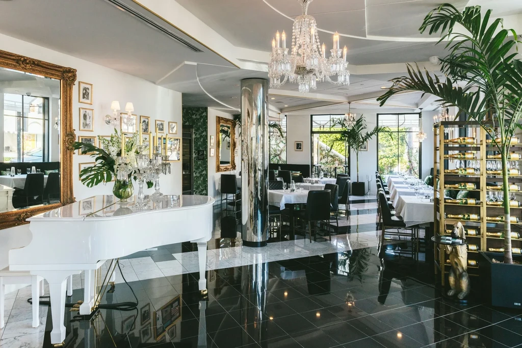 Grand piano, crystal chandelier, and polished floors in an elegant restaurant.