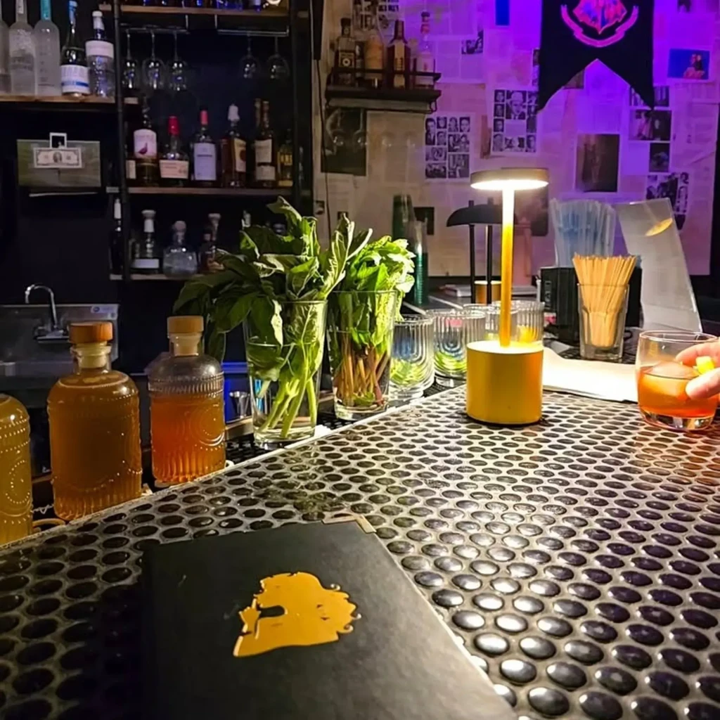 A hand holding a drink at a vibrant, dimly lit bar counter.
