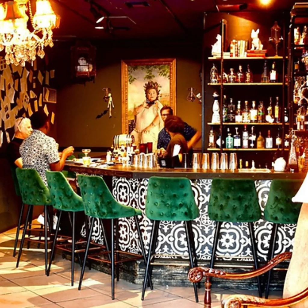 Ornate, dimly lit bar with green velvet stools and a gold portrait.