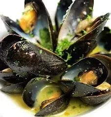 Close-up of steamed mussels in a white bowl with herbed sauce.