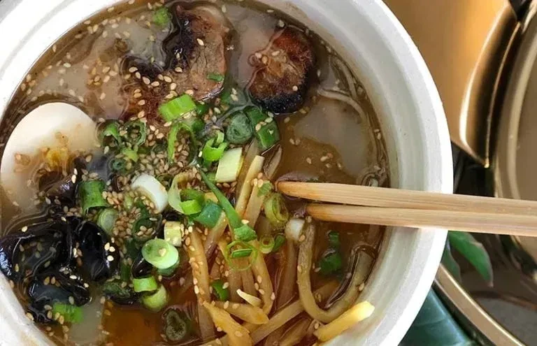 A ramen bowl from above, showing noodles, pork belly, egg, and chopsticks.