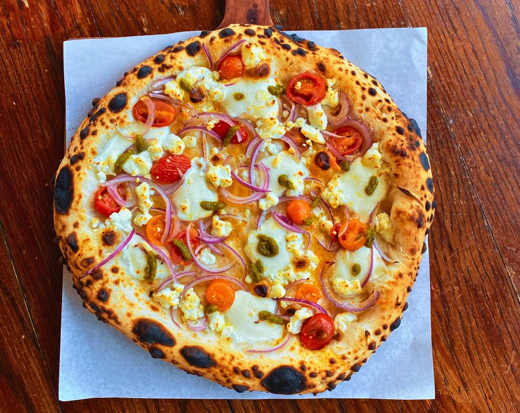 Neapolitan pizza with cheese, tomatoes, onion, pesto on wood.