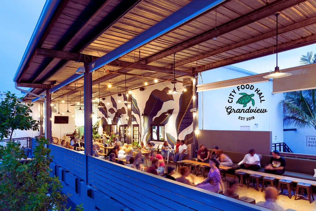 Lively City Food Hall patio at dusk, with patrons and warm lighting.