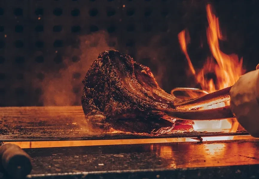 Crispy meat grilling over vibrant flames, manipulated by tongs.