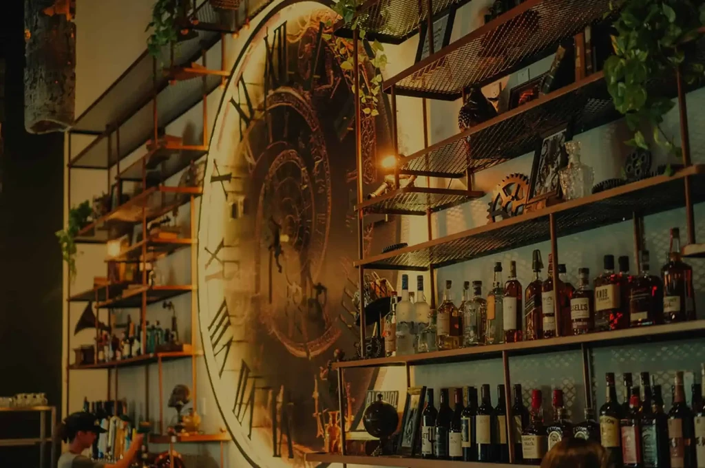 Steampunk bar with elaborate clock mural and industrial shelves of bottles.