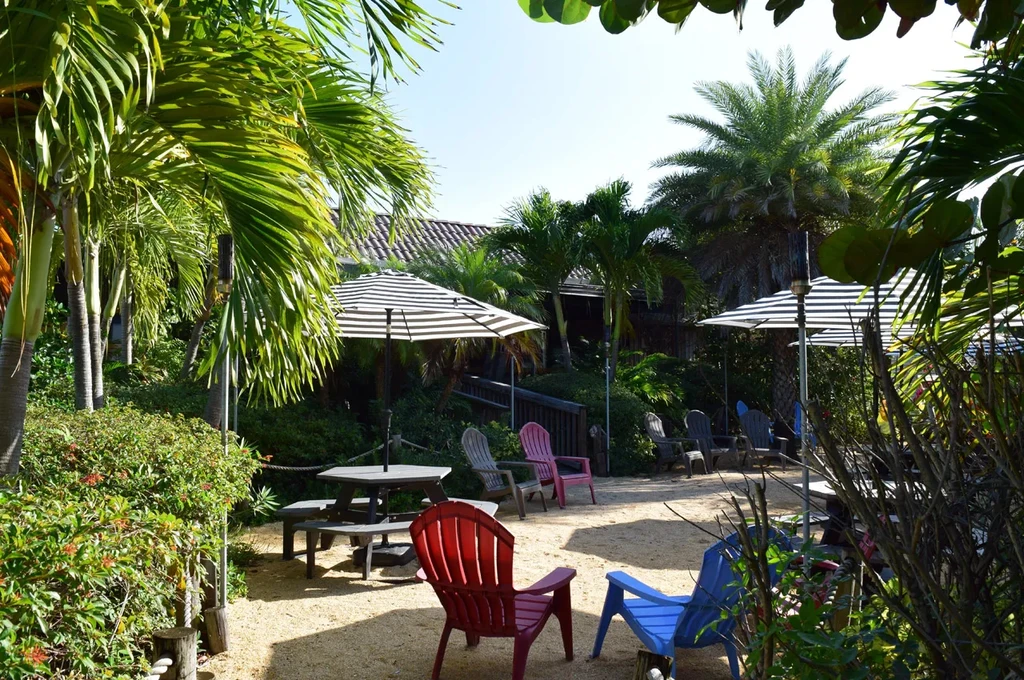 Sandy tropical outdoor dining area with picnic table and colorful chairs.