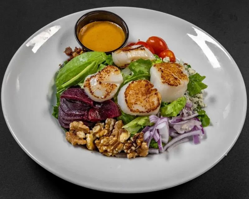 Plated salad with seared scallops, beetroot, avocado, blue cheese, and walnuts.