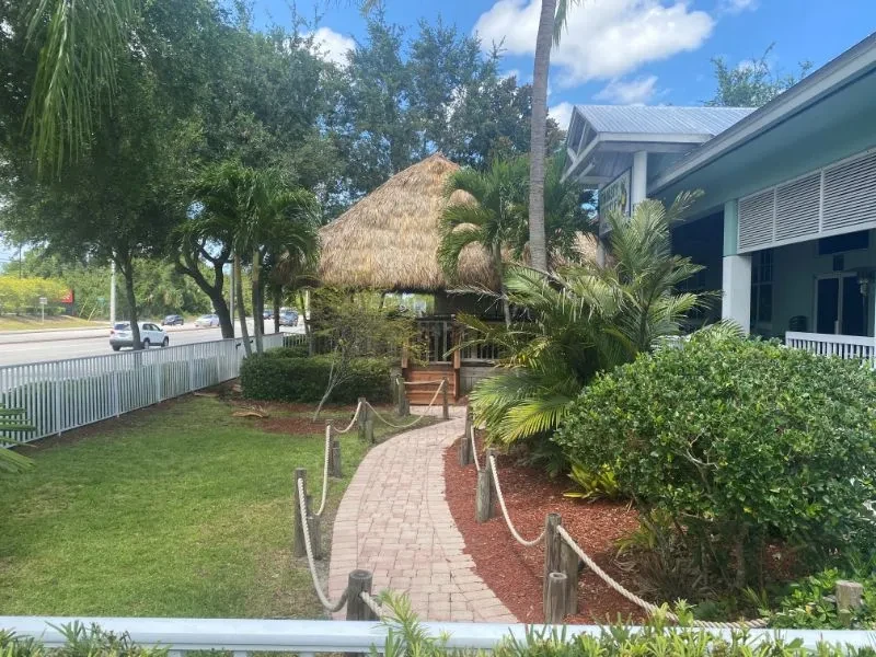 Outdoor tropical restaurant with tiki hut, brick path, and road.