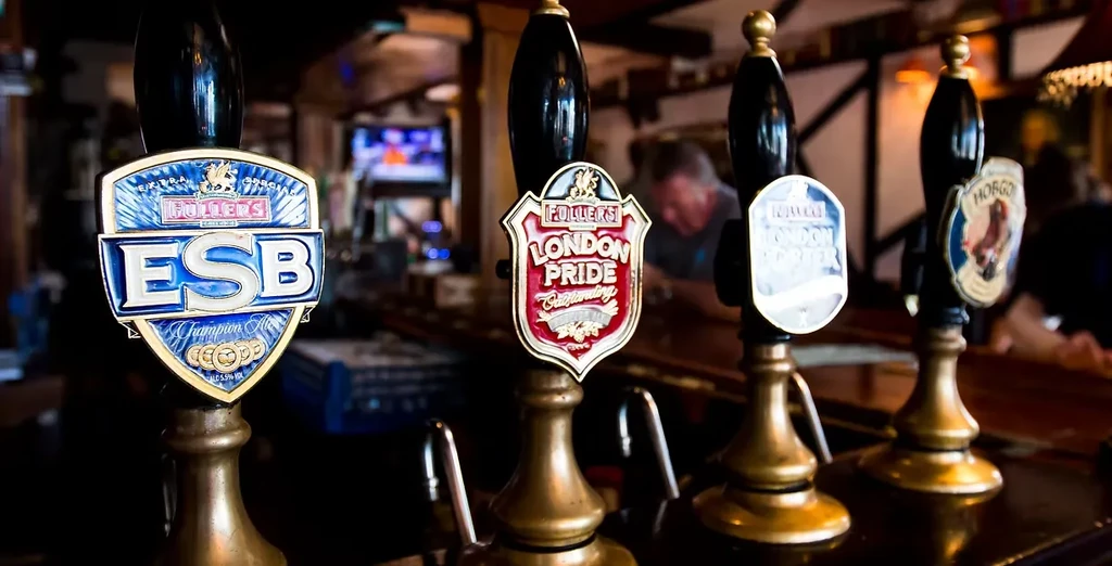 Four dark beer tap handles with Fuller's labels in a pub.