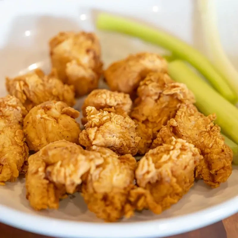 Crispy golden-brown boneless chicken wings with green celery sticks.
