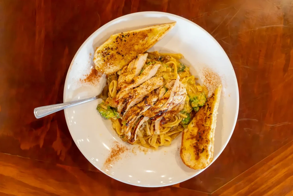 Plate of creamy pasta with grilled chicken, broccoli, and toasted bread.