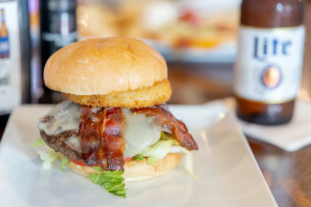 Close-up of hamburger with cheese, bacon, onion ring, and Miller Lite.