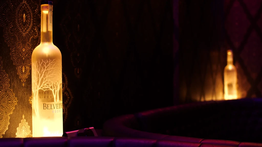 Glowing Belvedere Vodka bottle with frosted tree branches in a dim setting.