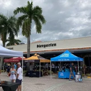 Outdoor market with tents, people, and palm trees by a biergarten.