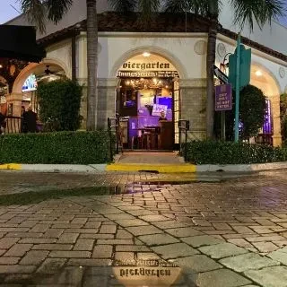 Biergarten building at night, with arches and sign reflected in puddle.