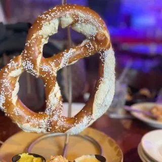 Golden-brown salted soft pretzel on a stand with dipping sauces.