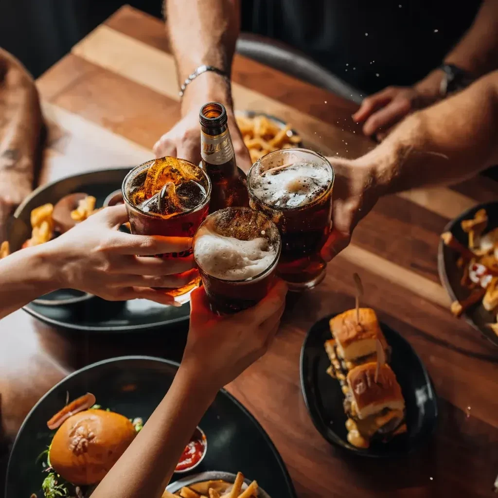 Overhead view of hands toasting drinks and food on a table.