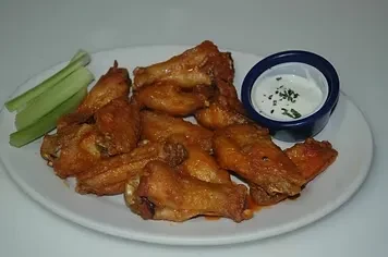 Buffalo chicken wings, celery, and creamy dip on a white plate.