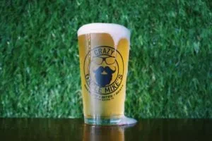 Pint glass of amber beer with overflowing foam and "Crazy Mike's" logo.